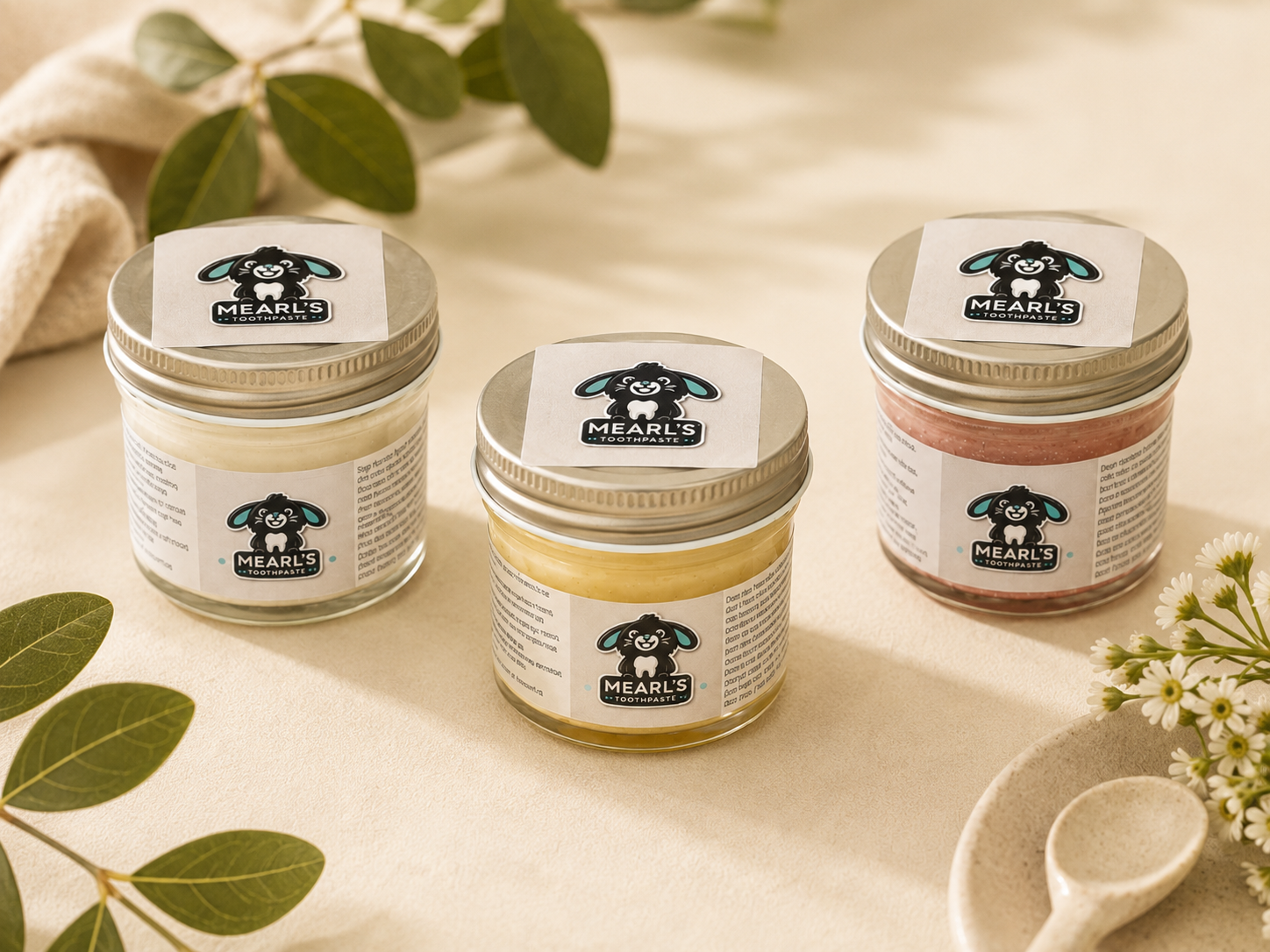 Mint, banana, and strawberry Mearl’s toothpaste jars arranged together.